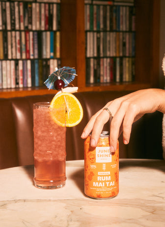 JuneShine Spirits Rum Mai Tai open can next to garnished clear cocktail glass.