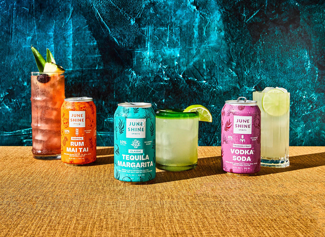 JuneShine Spirits cans and garnished cocktail glasses - left and right - Rum Mai Tai, Classic Tequila Margarita, Passion Fruit Vodka Soda.