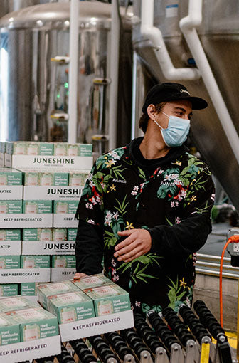 A man in a facemask loading pallets of JuneShine onto a moving belt