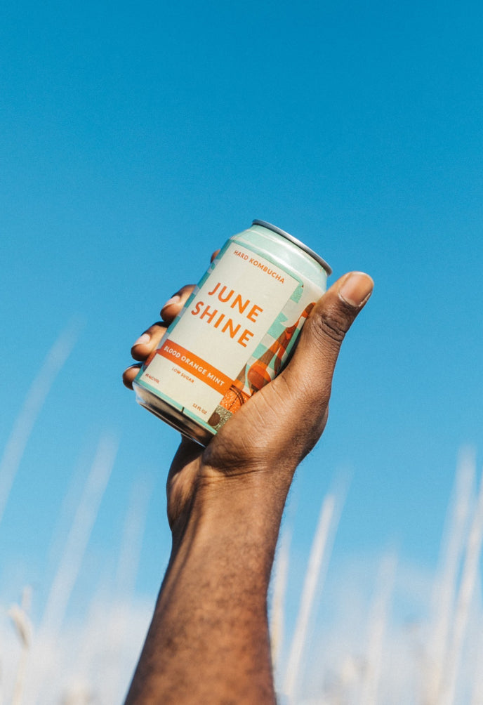 Hand holding a JuneShine can with a blue sky in the background