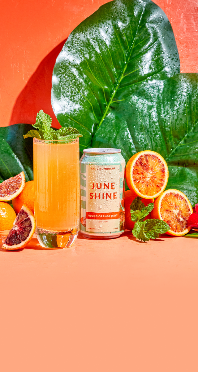 JuneShine Blood Orange Mint can next to full garnished glass surrounded by orange slices and leaves.