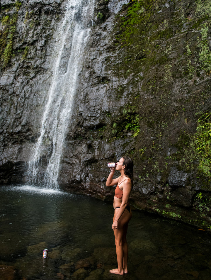 Woman drinking JuneShine at a waterfall in Hawaii