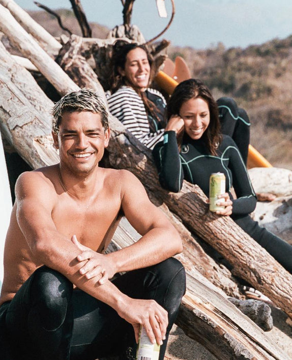 Surfer friends in wetsuits all enjoying cans of JuneShine at the beach