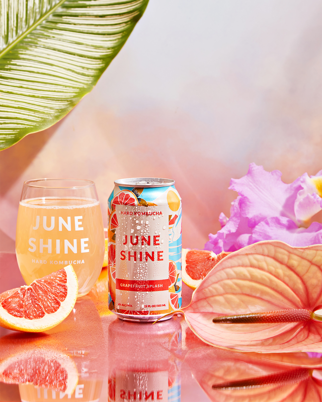 Grapefruit Paloma can in a dreamy pink setting with liquid poured in a JuneShine glass, a grapefruit slice, and pink flowers