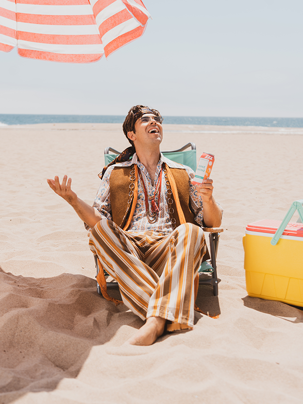 Cody Ko on the beach in a hippie costume with a can of Hippie Juice